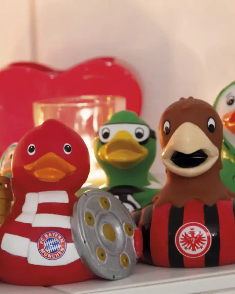 Badeenten in verschiedenen Vereinsfarben, eine davon mit Meisterschale