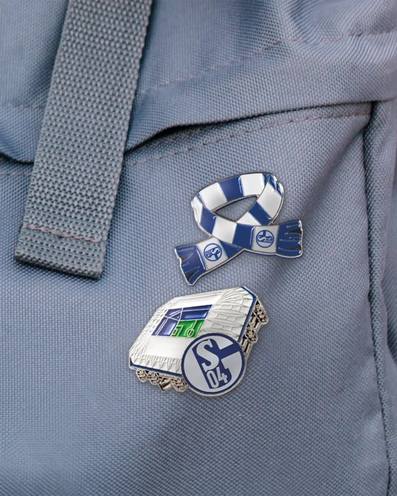 Zwei Anstecknadeln in Schal- und Stadionform an einem Rucksack